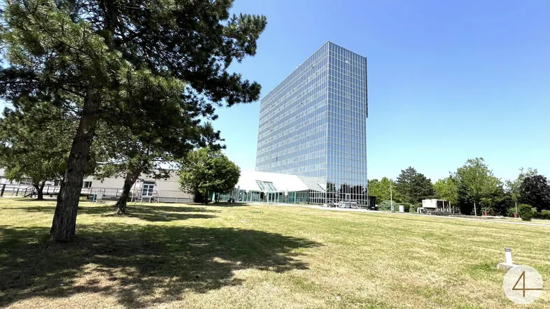 Modernes Bürogebäude mit Glasfassade und weitläufiger Grünfläche unter blauem Himmel.