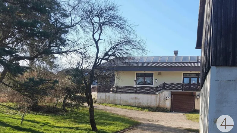 Ein Haus mit Photovoltaikanlage auf dem Dach, umgeben von Bäumen und einer Auffahrt.