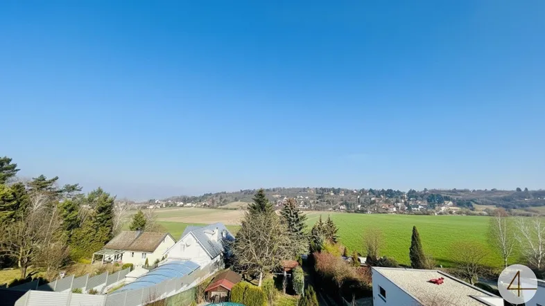 Weitläufiger Blick über grüne Felder und eine ländliche Siedlung unter klarem blauem Himmel.