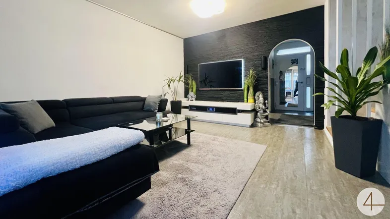 Modernes Wohnzimmer mit großer schwarzer Couch, dunkler Akzentwand und stilvoller Einrichtung.