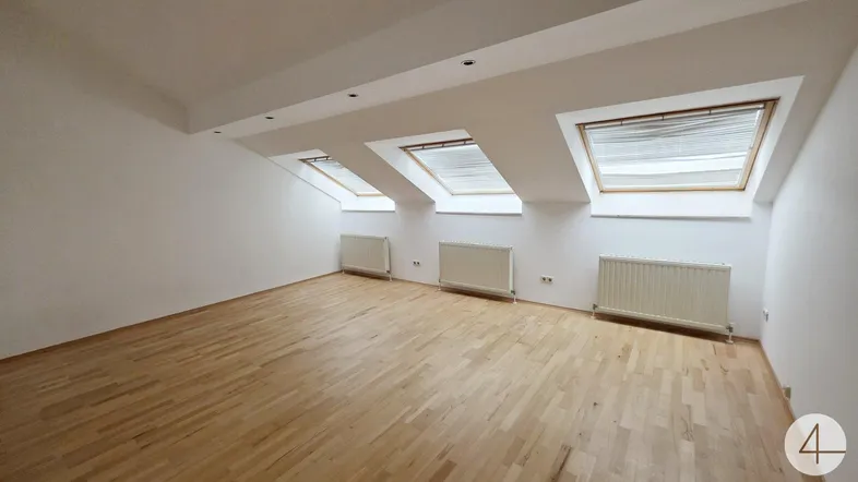 Helles Dachgeschosszimmer mit Holzfußboden, weißen Wänden und drei Dachfenstern, ideal als Wohn- oder Schlafbereich.