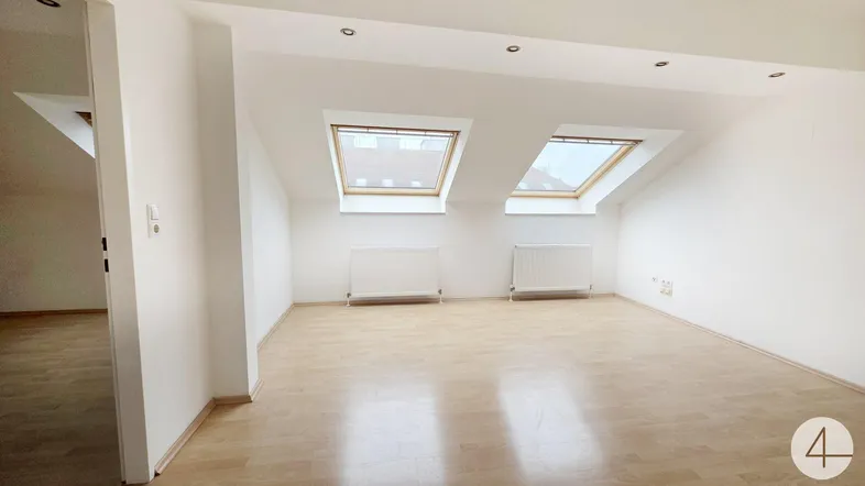 Helles Dachzimmer mit schrägen Wänden, zwei Dachfenstern und Laminatboden.