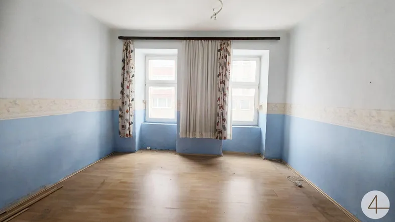 Helles Zimmer mit Holzboden und zwei Fenstern, bereit für eine Renovierung.