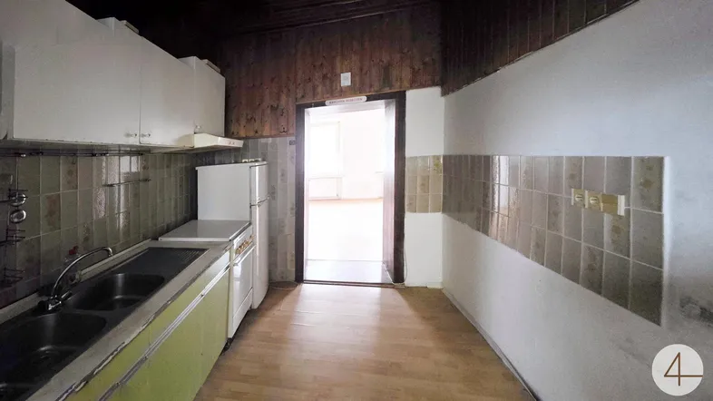 Küche mit älteren Einbaumöbeln, Fliesen und Holzwandverkleidung, bereit für eine Renovierung.