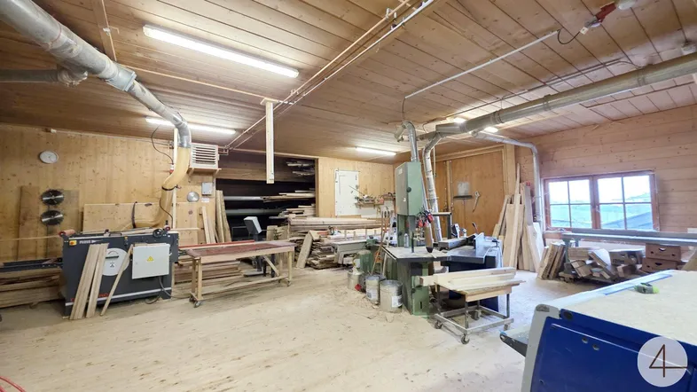 Geräumige Holzwerkstatt mit verschiedenen Maschinen, Holzmaterialien und natürlichem Lichteinfall durch Fenster.