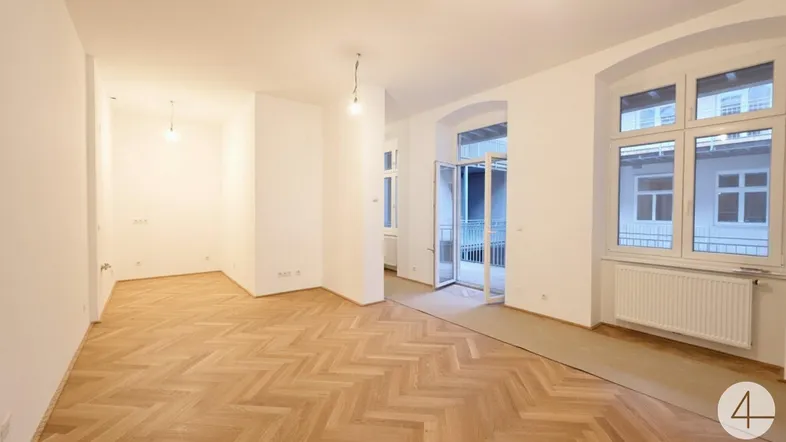 Helles, leeres Zimmer mit Fischgrätparkettboden und Zugang zu einem Balkon.