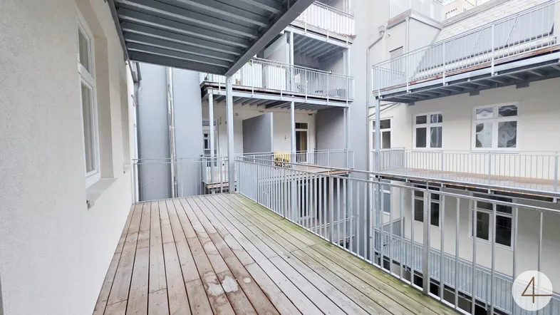 Geräumiger Balkon mit Holzboden und Metallgeländer, umgeben von weiteren Balkonen im Innenhof.