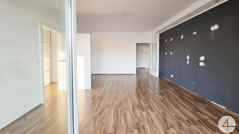 Geräumiges Wohnzimmer mit Laminatboden und einer teilweise gestrichenen Wand, bereit zur individuellen Gestaltung.
