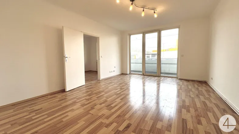 Helles Wohnzimmer mit Holzboden und Zugang zu einem Balkon, ideal für entspannte Stunden.