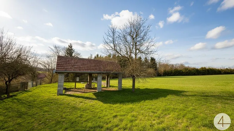 Offener Unterstand mit Ziegeldach auf einer grünen Wiese unter blauem Himmel, umgeben von Bäumen.