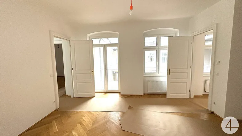 Helles, leeres Zimmer mit Fischgrätparkett und Zugang zu einem französischen Balkon.