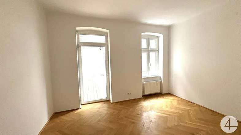 Helles Zimmer mit Parkettboden und einer Tür, die zu einem Außenbereich führt.