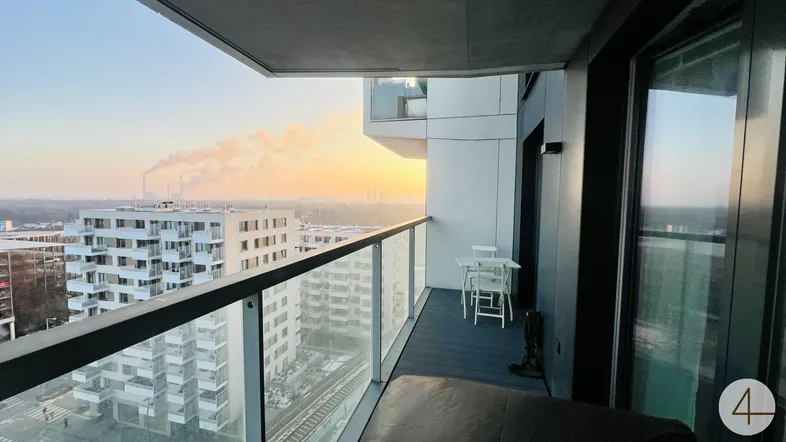 Geräumiger Balkon mit Glasbrüstung und weitem Blick über die Stadt bei Sonnenuntergang.
