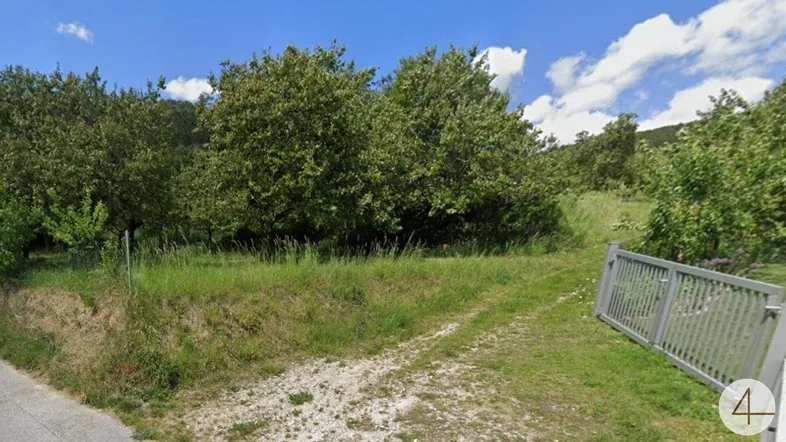 Grünes Grundstück mit Bäumen und einem einfachen Tor, umgeben von natürlicher Landschaft.