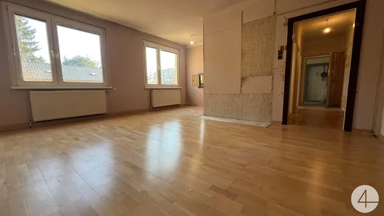 Geräumiges Wohnzimmer mit Parkettboden und mehreren Fenstern, bereit für Renovierung.