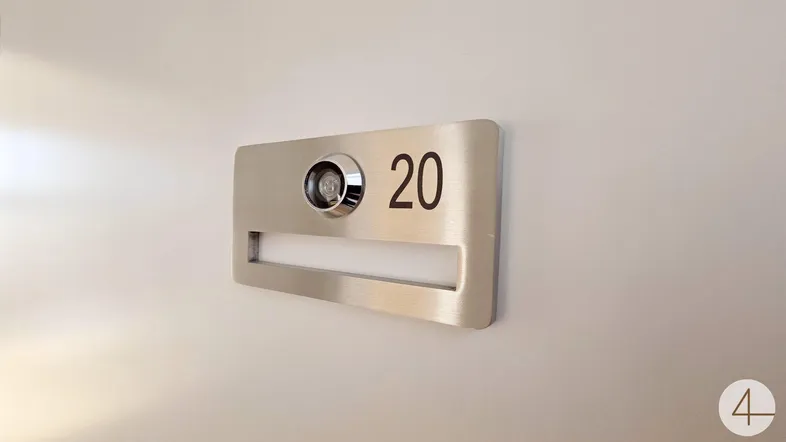 Modernes Türschild mit Wohnungsnummer 20, Türspion und Briefschlitz an einer weißen Wand.