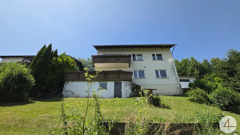 Rückseite des Hauses mit Balkonen und einem weitläufigen Gartenbereich mit Blick ins Grüne.