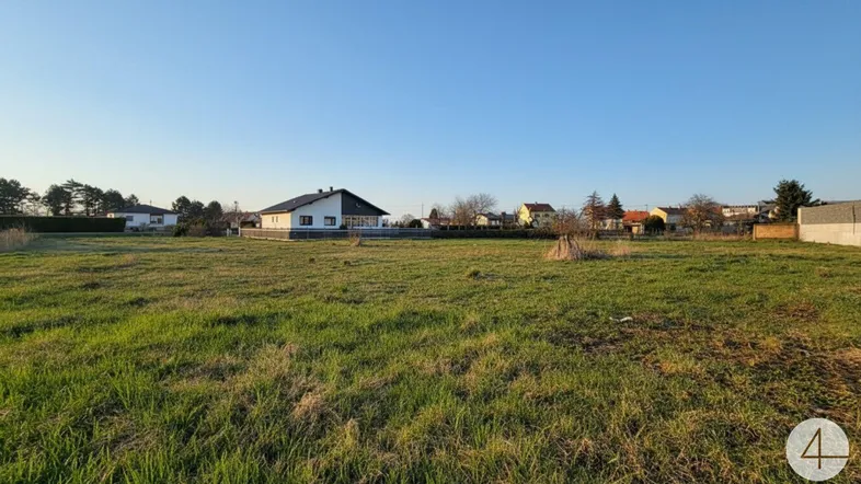 Weitläufiges Grundstück mit grüner Wiese und einem Einfamilienhaus im Hintergrund unter blauem Himmel.