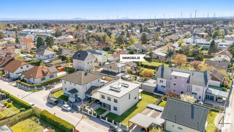 Luftaufnahme des modernen Einfamilienhauses in einer ruhigen Wohngegend mit Windrädern im Hintergrund.