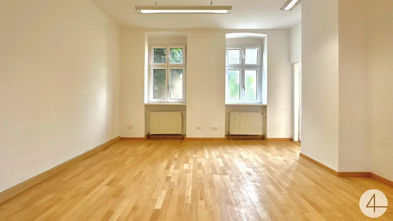 Heller, leerer Raum mit zwei Fenstern, Holzfußboden und Deckenleuchten, ideal als Bürofläche.