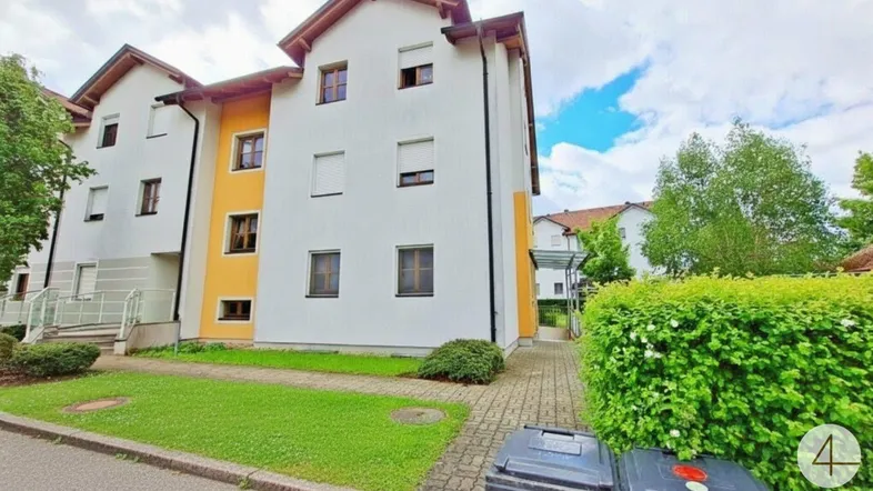 Mehrfamilienhaus mit weißer und gelber Fassade, umgeben von Grünflächen und Gehwegen.