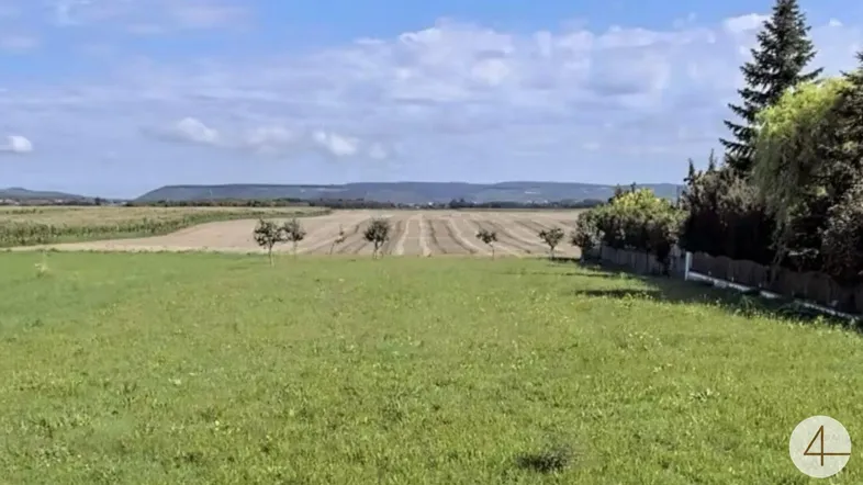 Weitläufige Grünfläche mit Blick auf Felder und Hügel unter blauem Himmel.
