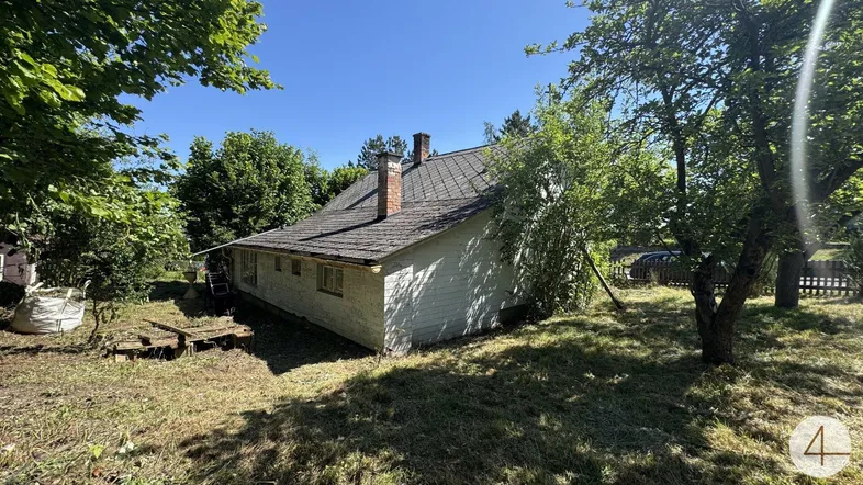 Älteres Einfamilienhaus mit Satteldach und Kamin, umgeben von Bäumen und Grünflächen.