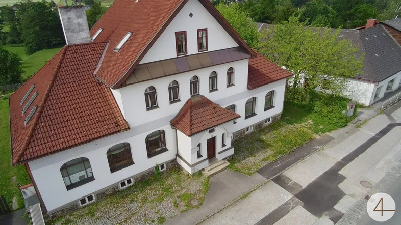 Luftaufnahme eines traditionellen weißen Gebäudes mit rotem Ziegeldach und gepflegter Fassade in ländlicher Umgebung.