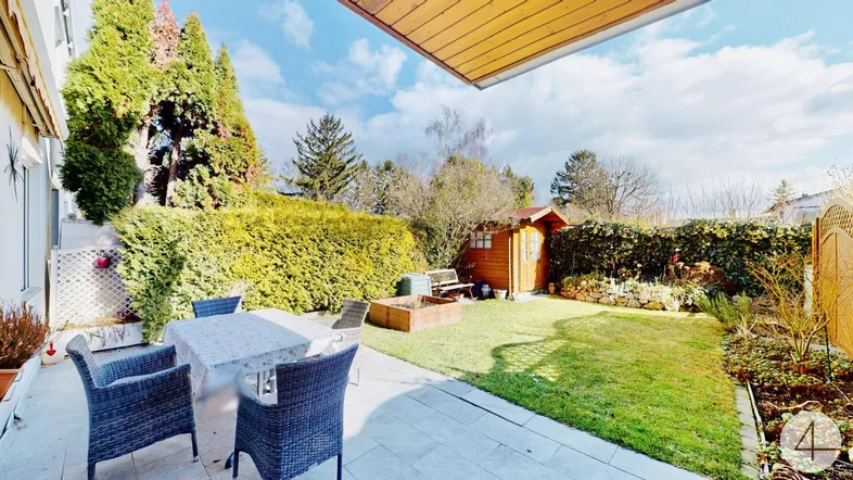 Große gepflasterte Terrasse mit Gartenmöbeln und Blick auf den gepflegten Garten mit Gartenhaus.