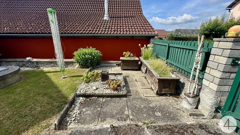 Kleiner Gartenbereich mit Rasenfläche, Betonplatten und Hochbeeten neben dem Haus.