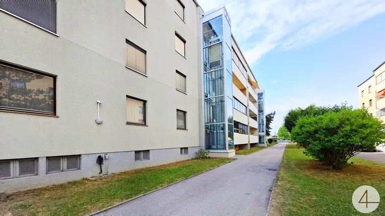Modernes Mehrfamilienhaus mit einem gläsernen Außenaufzug und gepflegter Grünanlage.