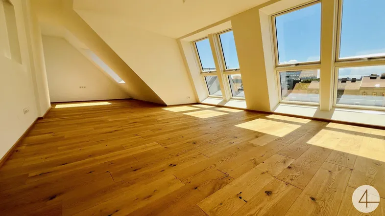 Heller Wohnraum im Dachgeschoss mit Holzboden und großen Fenstern, die viel Tageslicht hereinlassen.