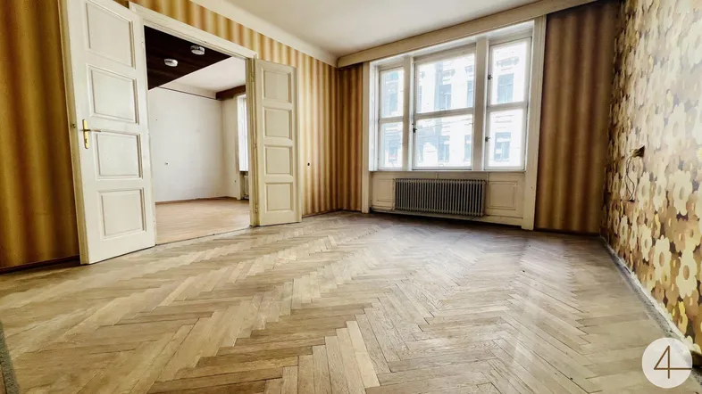 Geräumiges Zimmer mit Fischgrätparkett, großen Fenstern und Heizkörper, bereit zur Renovierung.
