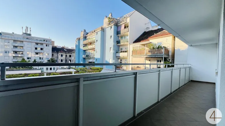 Langer Balkon mit Fliesenboden und Blick auf umliegende Wohngebäude bei Sonnenlicht.