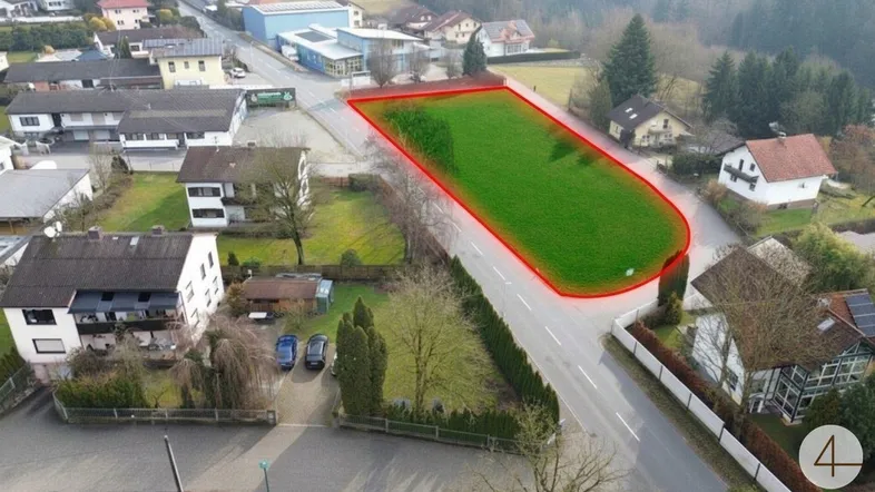 Luftaufnahme eines grünen Baugrundstücks in ländlicher Umgebung mit umliegenden Wohnhäusern und Straßenanbindung.