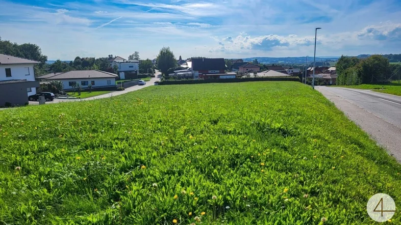Sonnige Grünfläche mit angrenzender Straße und weitem Blick über die ländliche Umgebung.