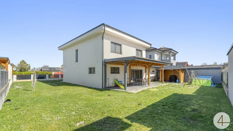 Modernes Einfamilienhaus mit großem Garten, überdachter Terrasse und Spielbereich für Kinder.