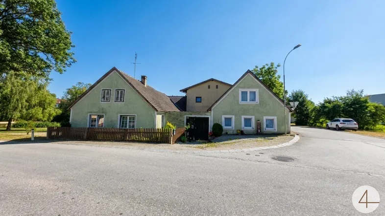 Vorderansicht eines traditionellen Hauses mit hellgrüner Fassade und Satteldach an einer Straßenecke.