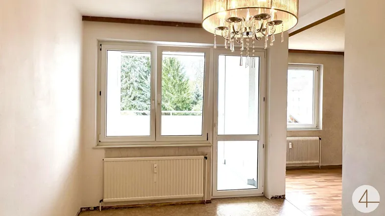 Heller Wohnraum mit großen Fenstern, Heizkörpern und einem eleganten Kronleuchter.