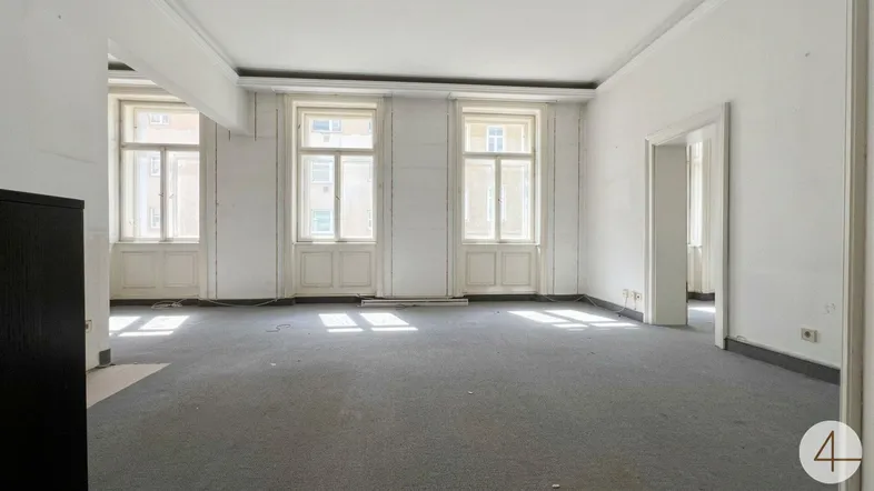 Heller, unmöblierter Raum mit Teppichboden und hohen Fenstern, bereit zur Renovierung.