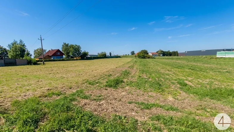 Weitläufiges Feldgrundstück unter blauem Himmel mit Blick auf umliegende Häuser und Natur.