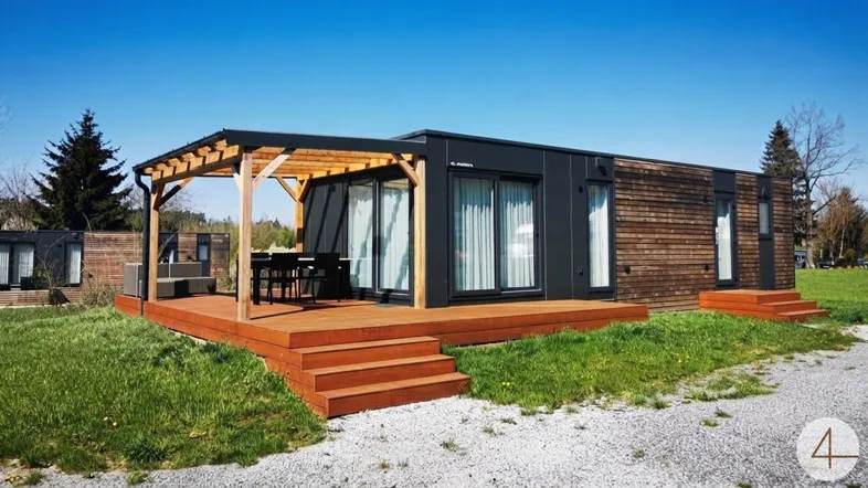 Moderne modulare Unterkunft mit großer Holzterrasse und Pergola im Grünen.