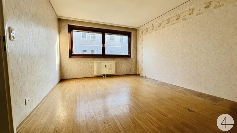 Leeres Zimmer mit Parkettboden, gemusterter Tapete und einem Fenster mit Blick auf Gebäude.