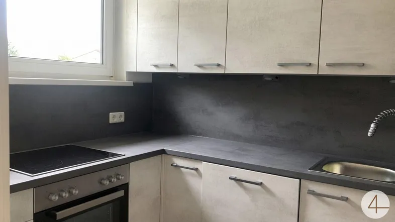 Moderne Küche mit hellen Schränken, dunkler Arbeitsplatte, Induktionskochfeld und Fenster.