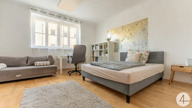 Helles Schlafzimmer mit Bett, Sofa, Schreibtisch und großem Fenster, ideal für Studenten oder Gäste.