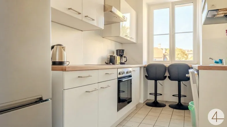 Helle Küche mit weißen Schränken, Holzarbeitsplatte und Fenster mit Blick nach draußen.