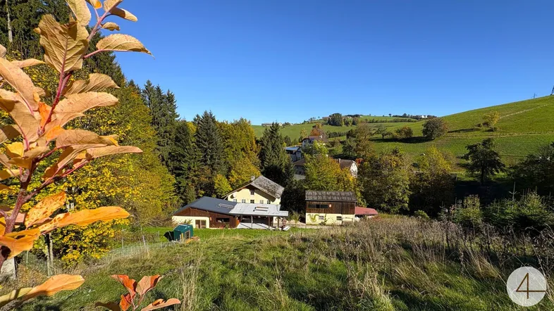 Ländliche Ansicht des Anwesens umgeben von grünen Hügeln und herbstlichen Bäumen unter blauem Himmel.