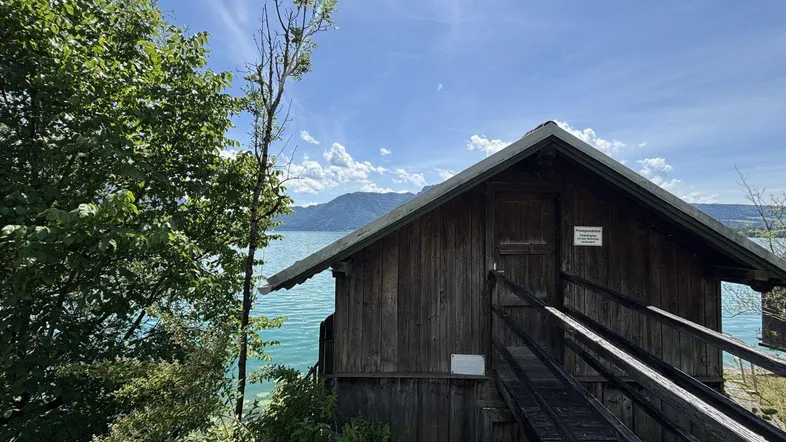 Rustikales Holzbootshaus am Seeufer mit Blick auf die umliegenden Berge und grüne Natur.