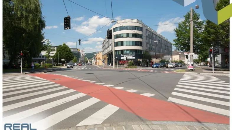 Blick auf eine belebte Straßenkreuzung mit einem modernen Geschäftsgebäude und viel Tageslicht.