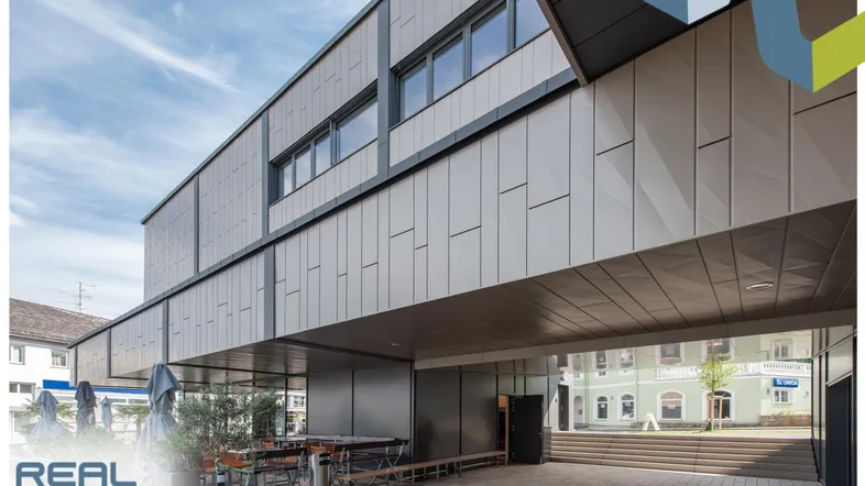 Moderne Geschäftsfassade mit geometrischen Paneelen und einem überdachten Außenbereich mit Sitzgelegenheiten.